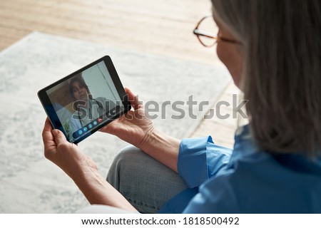 Over shoulder closeup view of old woman patient video calling virtual doctor using tablet at home. Online telemedicine chat meeting. Seniors ehealth, telehealth consultation, tele medicine concept. Royalty-Free Stock Photo #1818500492