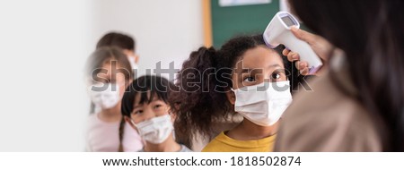 Teacher using digital thermometer for check temperature measurement on African American girls forehead. Diversity students in face mask with COVID-19 Screening in the classroom at Elementary school Royalty-Free Stock Photo #1818502874