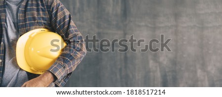 Construction worker Holding yellow helmet on a Cement wall with copy space for banner Royalty-Free Stock Photo #1818517214