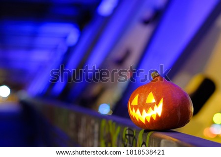 Halloween pumpkin in the dark on a blue industrial abstract background. Blurry colored lights. The decor of the night city in a festive Halloween theme. Copy space.