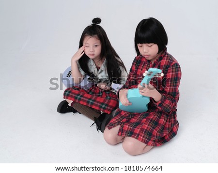 Two sisters sitting on ground floor,hold ukulele in hands with interested feeling,doing activity together