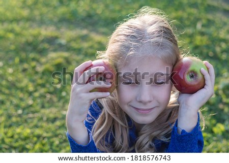 soft focus. Daylight. A girl with white hair holds two red apples in her hands. The sun is low.