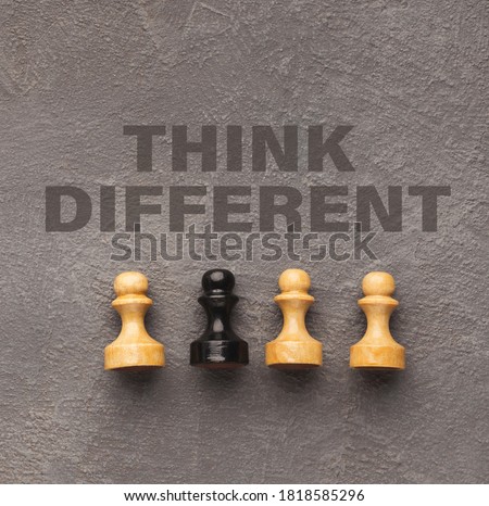 One black pawn among wooden ones over grey background, think different lettering above, collage