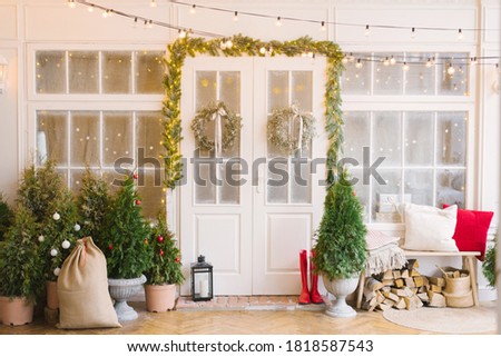 The Christmas porch is decorated with small Christmas trees and lanterns. Bench with pillows near the front door of the house Royalty-Free Stock Photo #1818587543