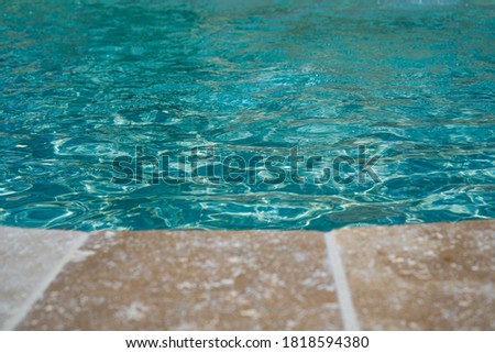 Open swimming pool edge, water and beige marble texture. Vacation, holiday. Ripple water. Water color abstract texture. Swimming pool water sun reflection background. Selective focus