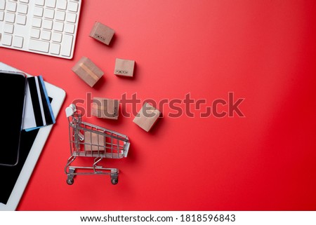 Online shopping,paper boxes,small shopping cart,smartphone, credit card and keyboard against red background