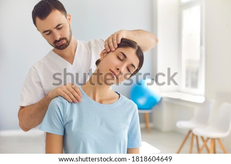 Licensed chiropractor or manual therapist doing neck stretch massage to relaxed female patient in clinic office. Young woman with whiplash or rheumatological problem getting professional doctor's help Royalty-Free Stock Photo #1818604649