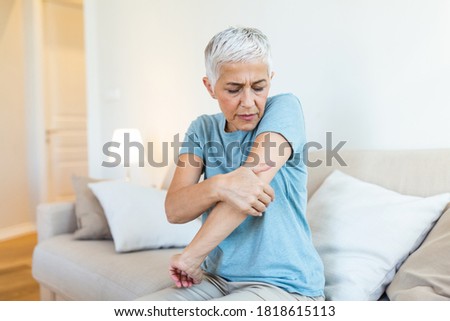Old age, health problem and people concept - close up of senior woman suffering from pain in hand at home. woman hand holding her elbow suffering from elbow pain. Royalty-Free Stock Photo #1818615113