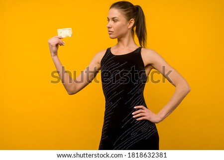 Photo of pleased young woman posing isolated over yellow wall background holding debit or credit card.