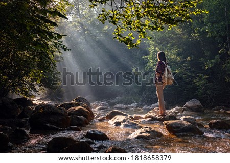 A woman explores new, magical, and fantastic places around the world, surrounded by nature and spreading her arms to breathe and relax. Female hiker crossing the forest creek. Royalty-Free Stock Photo #1818658379