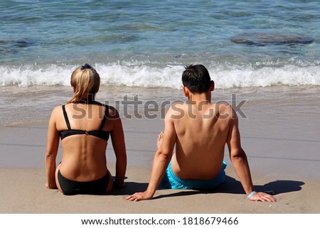Couple sitting on a sand on azure sea background. Man and girl in bikini together, romantic holiday and beach vacation