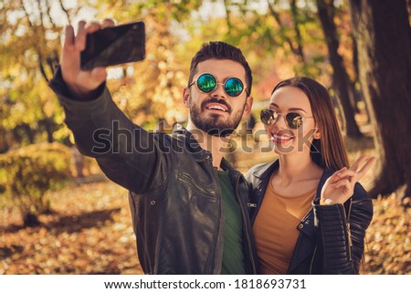 Photo of two people students girl guy take selfie on cellphone make v-sign in fall september season park wear glasses jacket