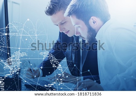 Portrait of two young businessmen working with laptop in blurry office with double exposure of network interface. Toned image