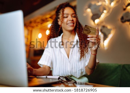 Сredit card in female hand. African American woman sitting at cafe making online shopping. Online shopping, e-commerce, internet banking, spending money.
