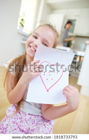 Happy girl shows a sheet of paper with a red heart