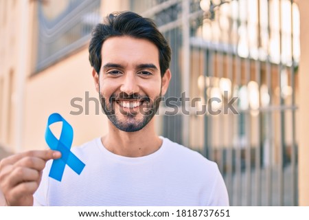 Young hispanic man smiling happy holding blue ribbon at the city. Royalty-Free Stock Photo #1818737651