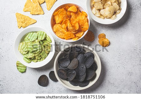 Different types of potato chips in white bowls, gray background. Fast food concept.