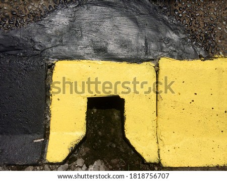 Concrete road divider with drainage holes combined with gravel, painted black and yellow. Closeup image of concrete street block