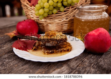 Basket with apples and grapes, ceramic dish with honeycombs and honey, autumn leaves on a wooden background.