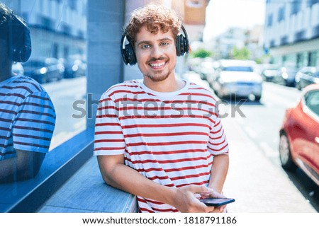 Young caucasian man smiling happy listening to music using headphones and smartphone leaning on the wall at city.