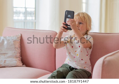 Beautiful little girl playing game or watching video on smartphone mobile. Girl watching cartoons or browsing internet, copy space. Side view portrait of little girl using smartphone while sitting on 