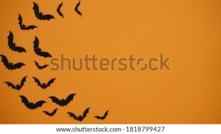 Halloween holiday concept. Black paper bats on bright orange background, top view, flat lay,copy spaes.Celebration of the dead.