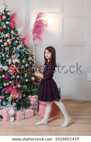 A seven-year-old dark-haired girl near a Christmas tree. vertical photo