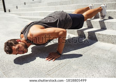 Young man exercising outside. Picture of guy doing push up exercises on steps. Guy keeps legs on stairs and hands on ground. Urban training alone.
