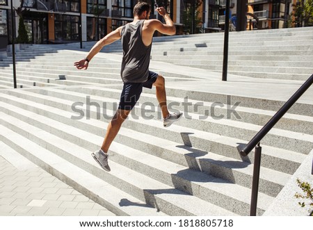 Young man exercising outside. Side back view of strong fast guy jumping up several steps outside on street. Powerful athletist training or having workout. Growing up body strenght.