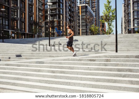 Young man exercising outside. Picture of guy running or jogging alone outside near steps. Urban city view. Slow or fast running. Exercising or training outside during daylight and summertime.