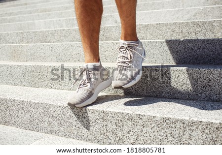 Young man exercising outside. Picture of man's feet in sneakers walking down steps outside duing sunshine or daylight. Small training exercising on street. Shade from legs.
