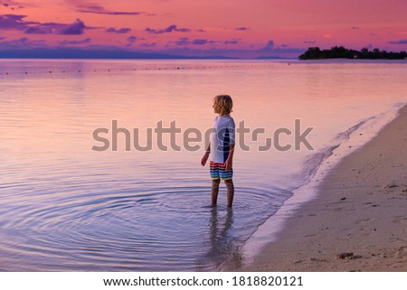 Child playing on ocean beach. Kid jumping in the waves at sunset. Sea vacation for family with kids. Little boy on tropical beach of exotic island on summer holiday. Sunset view. Sand and water fun.