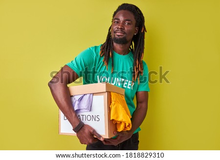 portrait of black afro volunteer man with box full of clothes, young male with dreadlocks engaged in charity, love helping others