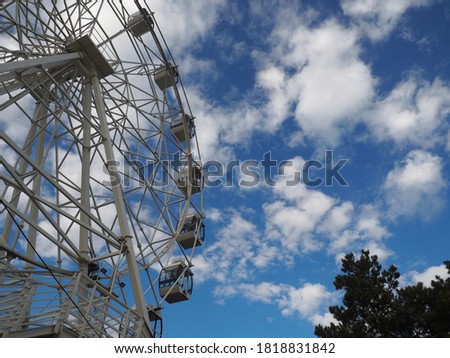 round white ferris wheel with empty deserted cabins in the park, blue sky with clouds, bottom side angle view