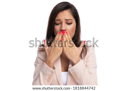 Closeup of upset businesswoman covering her mouth and looking down while standing on white studio background