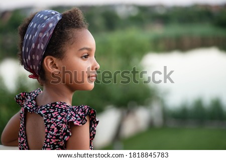 Portrait of beautiful mixed race kid in nature. Beautiful profile. Soft light. Afro hair. Child looks to the side. Concept of childhood, travel, future, dreams, peace. Copy space. Young girl outdoor. Royalty-Free Stock Photo #1818845783