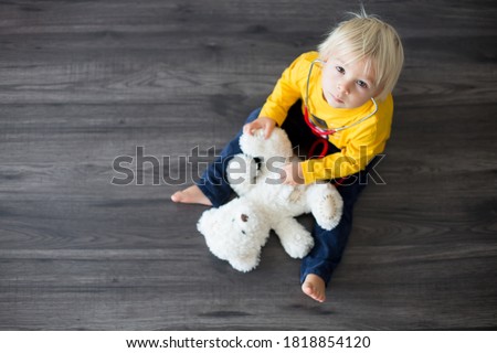 Sweet toddler child, playing doctor, examining teddy bear toy at home, isolated background