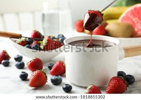 Dipping strawberry into fondue pot with chocolate on white marble table Royalty-Free Stock Photo #1818855302