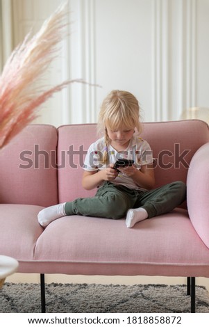Beautiful little girl playing game or watching video on smartphone mobile. Girl watching cartoons or browsing internet, copy space. Side view portrait of little girl using smartphone while sitting