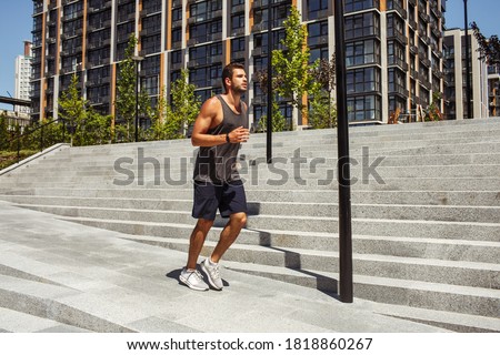 Young man exercising outside. Guy jogging or slow running besides steps. Training or having workout outside. Exercsing on fresh air during summertime. Healthy lifestyle.