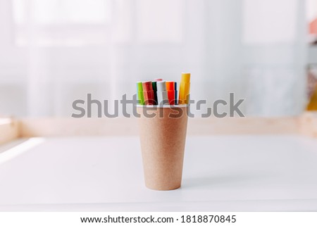 Colorful marker pens in the craft paper jar on white table. School supplies.