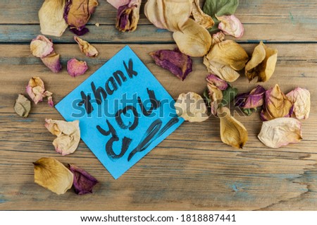 dried roses and blue paper on wooden wall with the words thank you.