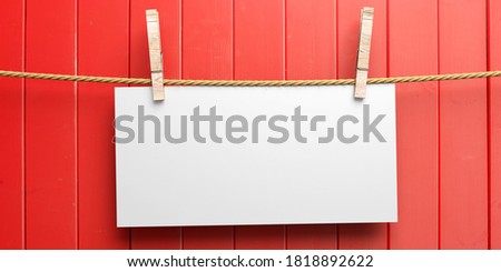 Empty paper card holding on rope with two clothespins on red wooden background. Blank memo, reminder, sign template. 3d illustration
