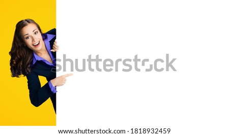 Happy excited woman in black confident suit, violet blouse showing pointing blank banner signboard. Business and advertising concept. Copy space empty place for text. Yellow orange colour background.
