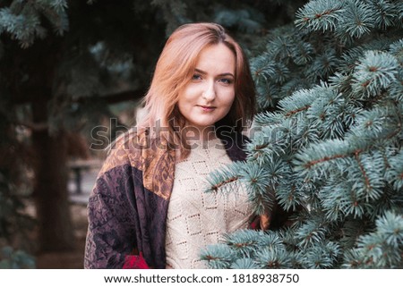Young, green-eyed blonde posing in the park, against the background of Christmas trees, in the winter season. Photo taken in January