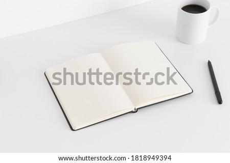 Open notebook mockup with a cup of coffee and a pen on a white table.