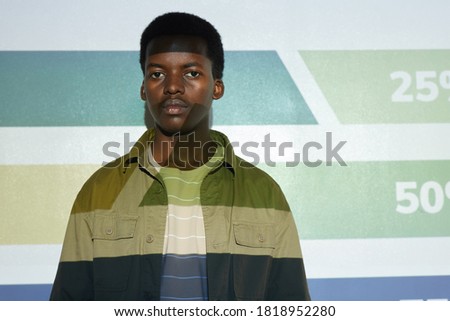 Waist up portrait of young African-American man standing by projector screen with stripes and numbers on it, copy space