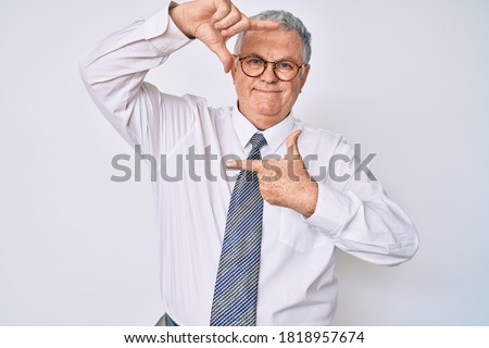 Senior grey-haired man wearing business clothes smiling making frame with hands and fingers with happy face. creativity and photography concept. 