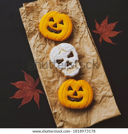 Creepy funny skull shaped and pumpkin Halloween cookies filled with chocolate and dry autumn leaves on black wooden background. Top view, flat lay. Holiday pastry.