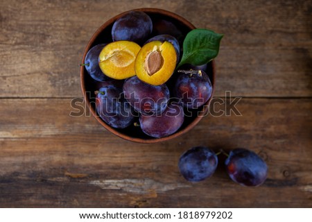 Blue plum in a bowl on a wooden table. Plums in a cut. Top view, place for text. Fruit background with copy space. Still life food. Royalty-Free Stock Photo #1818979202